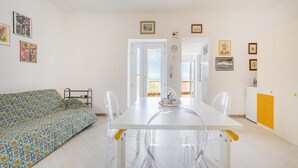 A modern living room with a patterned sofa, a white dining table with clear chairs, and a balcony visible through the door. - Terramare Guesthouse (Procida)