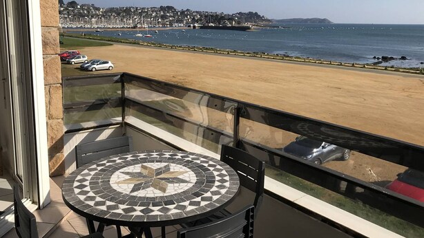 A balcony with a tiled table and chairs, overlooking a beach and a marina. - Apartment with terrace and WIFI in Perros-Guirec (Perros-Guirec)