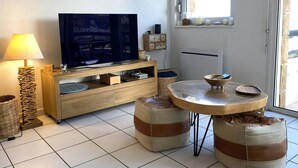 A living room with a TV, wooden furniture, a lamp, and a window with a view. - Apartment with terrace and WIFI in Perros-Guirec (Perros-Guirec)