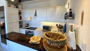 A modern kitchen with white cabinets, a black countertop, and a microwave. There are two woven baskets on the counter. - Apartment with terrace and WIFI in Perros-Guirec (Perros-Guirec)