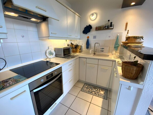 A modern kitchen with white cabinets, a black stove, a microwave, and a sink.
