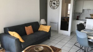 A modern living room with a dark grey sofa, yellow cushions, a wooden coffee table, and a dining area with a blue chair and plates. - Apartment with terrace and WIFI in Perros-Guirec (Perros-Guirec)
