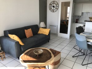 A modern living room with a dark grey sofa, yellow cushions, a wooden coffee table, and a dining area with a blue chair and plates.