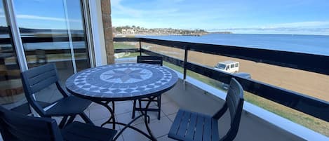 A balcony with a round table and four chairs, overlooking a beach and ocean.