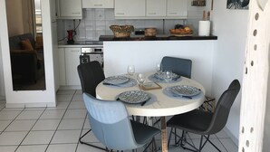 A modern kitchen with white cabinets, a dining table set with plates and glasses, and a living area with a sofa and a TV. - Apartment with terrace and WIFI in Perros-Guirec (Perros-Guirec)