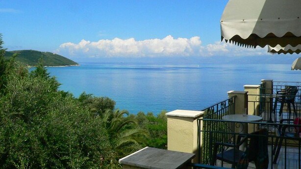 A seaside view with a balcony, outdoor seating, and a clear sky.