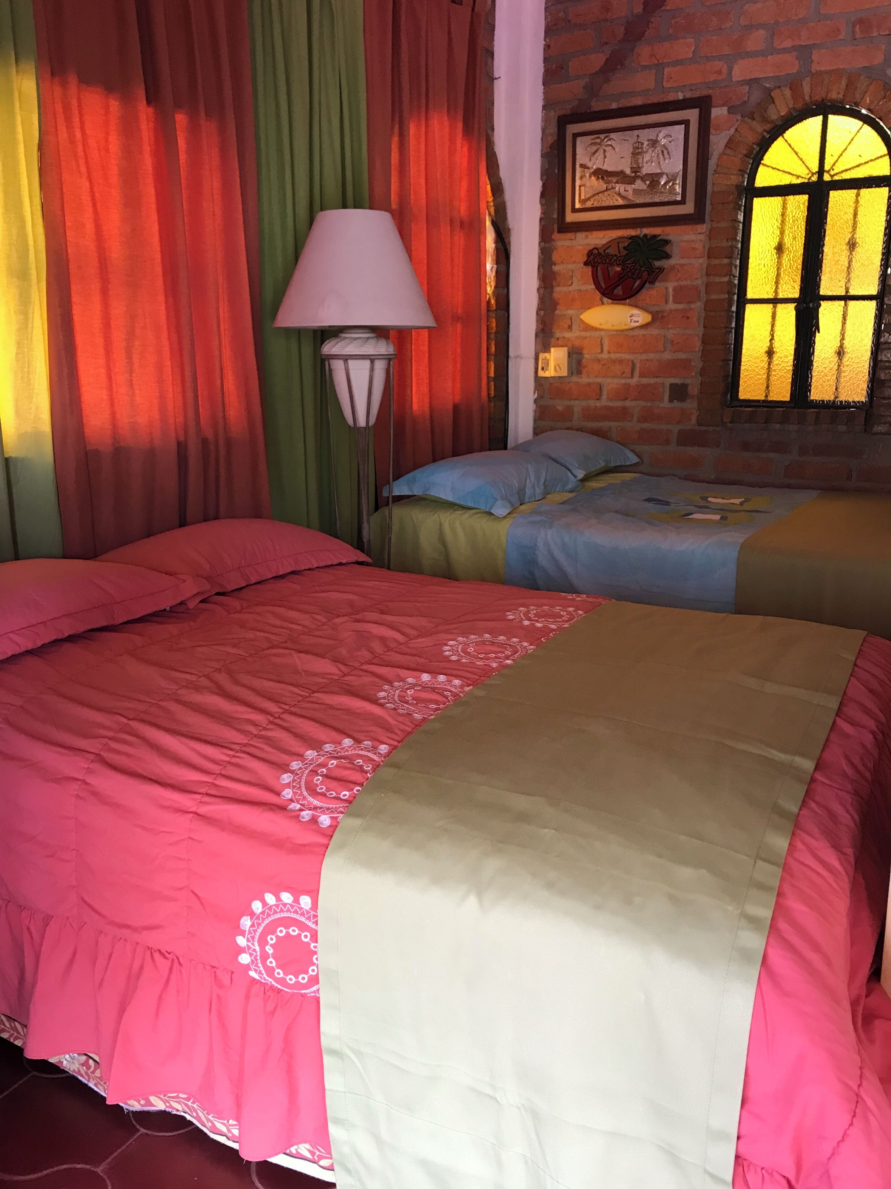 A room with two beds, a lamp, and a brick wall with a picture.