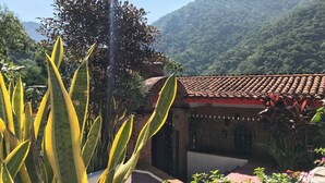 Ein Innenhof mit Ziegeldach, umgeben von üppiger Vegetation und einem Blick auf die Berge.