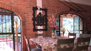 Ein Essbereich mit Backsteinwand, einem Tisch mit Blumenmuster-Tischdecke, Stühlen, einer Vase mit Blumen und einem dekorativen Spiegel.