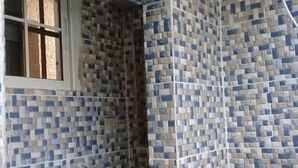 Ett badrum med väggar beklädda med mosaik, ett fönster och en dusch.
