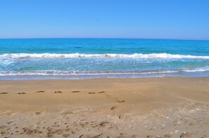 A beach with footprints leading to the water, a clear sky, and calm waves.