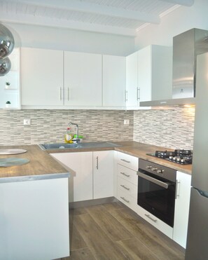 A modern kitchen with white cabinets, a tiled backsplash, a stainless steel sink, and a built-in oven.