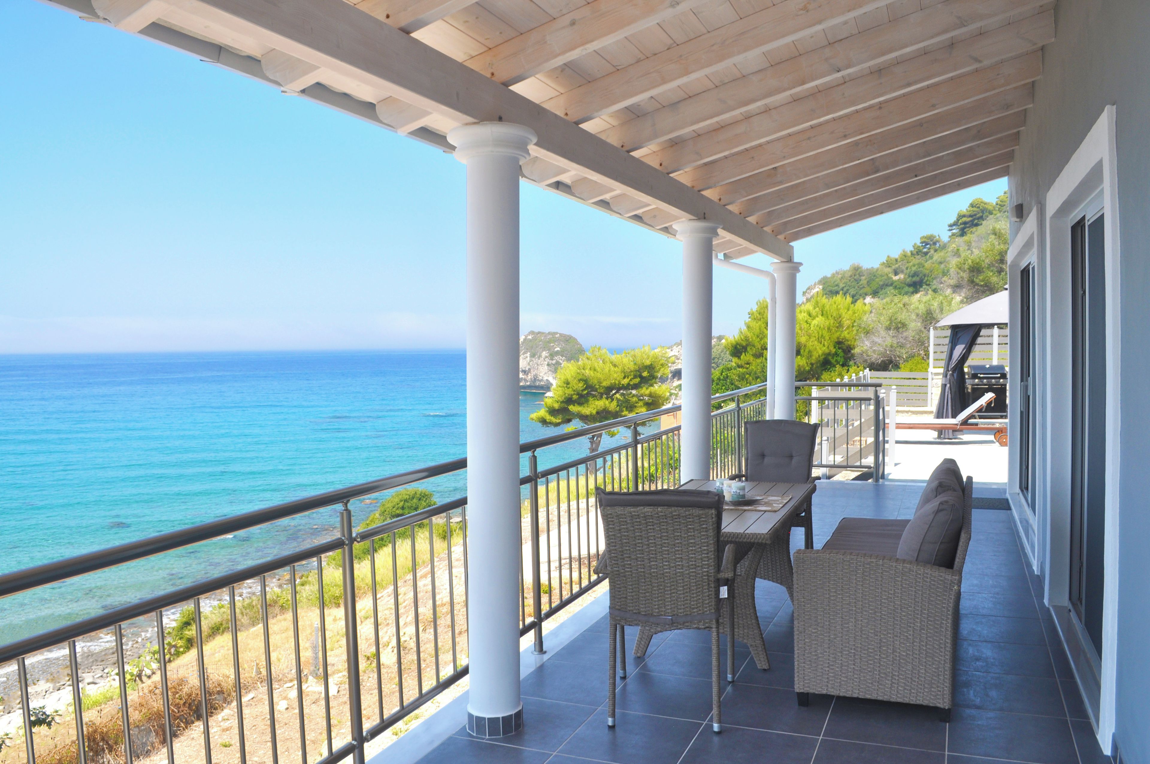 Un espace extérieur abrité, aménagé avec une table et des chaises, et offrant une vue sur la mer.