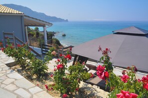 A coastal terrace with a view of the sea, a covered seating area, and a stone pathway. - Villa Philippos on Dechoumenes Beach - Agios Gordios, Corfu (Corfu)