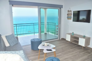 A modern living room with a view of the ocean, a sliding glass door, a sofa, a coffee table, and a TV mounted on the wall. - Villa Philippos on Dechoumenes Beach - Agios Gordios, Corfu (Corfu)