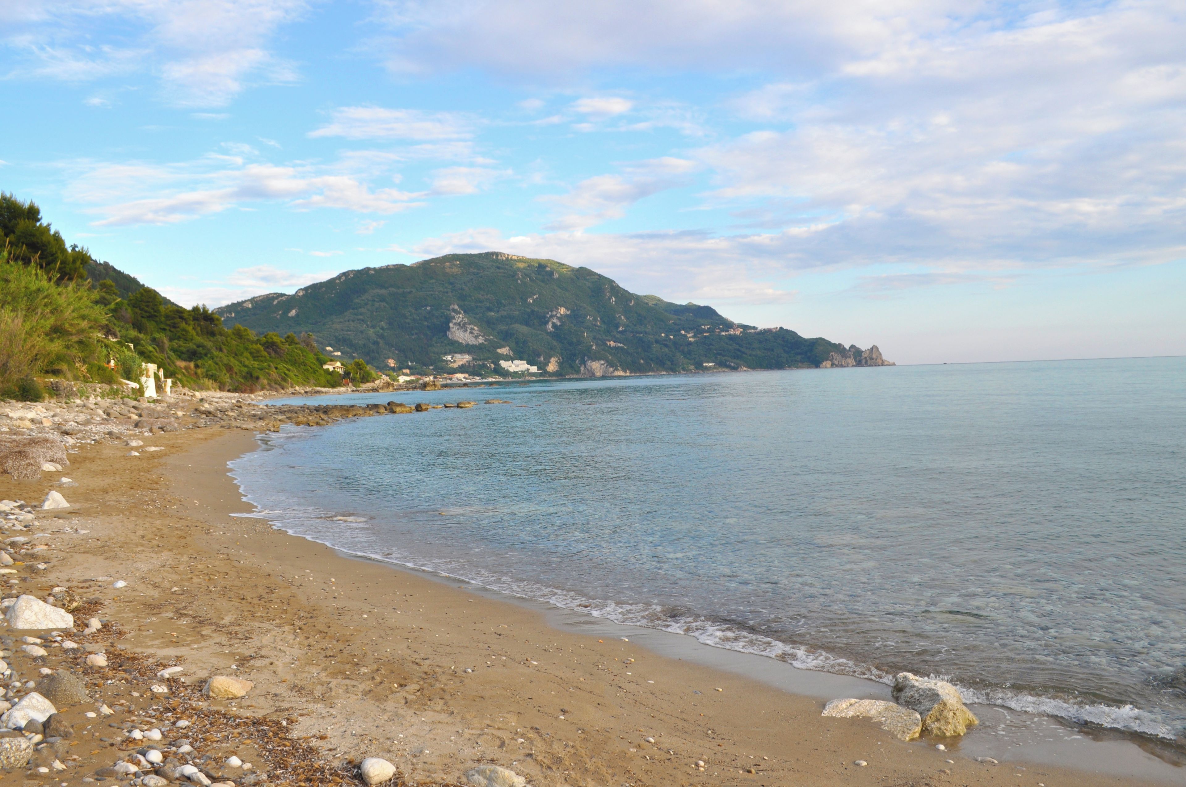 A beach with a rocky shoreline, calm water, and a mountain in the background.