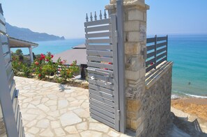 Ein gepflasterter Weg führt zu einem ehrfurchtgebietenden Eingang mit Blick auf einen Strand, kristallklares blaues Wasser und ferne Berge.