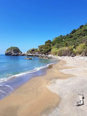 Ein Strand mit klarem, blauem Wasser, Sandstrand und Felsformationen.