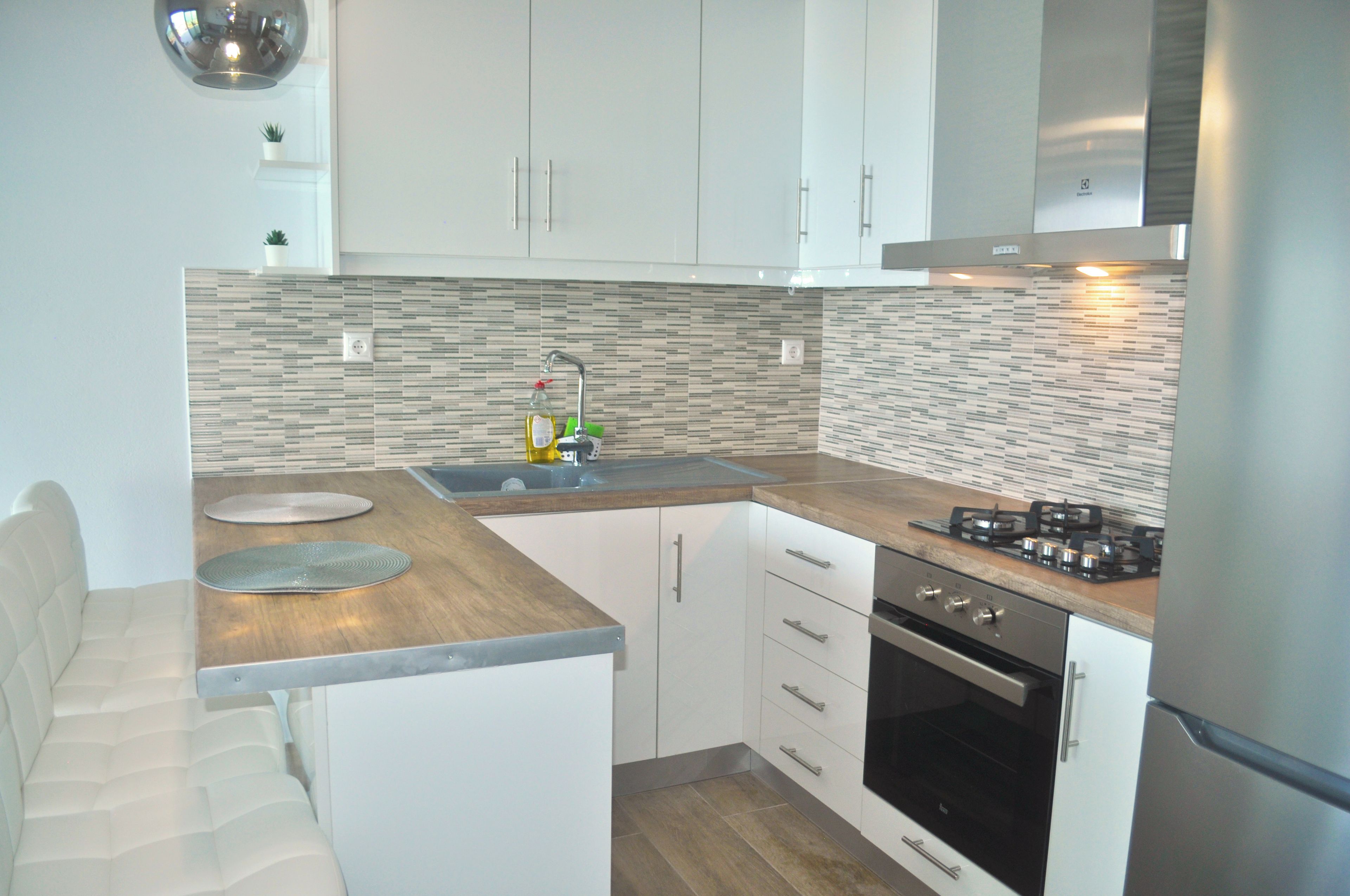 Een moderne keuken met witte kastjes, een roestvrijstalen afzuigkap en een betegelde spatwand.