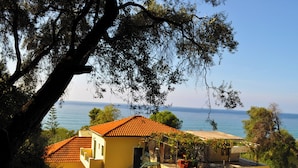 A yellow building with a red-tiled roof, a staircase, and a view of the sea. - Holiday House Angelos A on Agios Gordios Beach (Corfu)