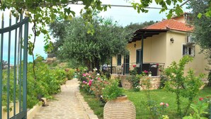 A stone pathway leading to a house with a tiled roof, surrounded by lush greenery and flowering plants. - Holiday House Angelos A on Agios Gordios Beach (Corfu)