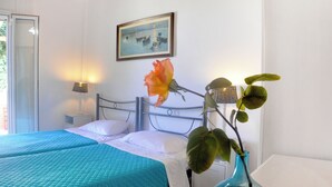 A hotel room with two beds, a nightstand, a vase with a flower, and a painting on the wall. - Holiday House Angelos A on Agios Gordios Beach (Corfu)