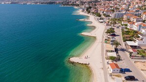 Vista aérea de un pueblo costero con una extensa playa de arena, aguas azules cristalinas y edificios residenciales a lo largo de la costa.