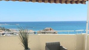 En balkong med möbler i rotting, en krukväxt och utsikt över havet.