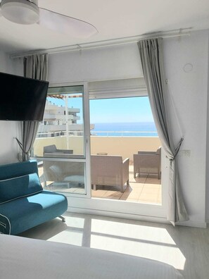 Enjoy the ocean view from your balcony, featuring a sofa and chairs, flat-screen TV, and ceiling fan.