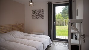 Un dormitorio con dos camas, una mesita de noche pequeña, un aplique y una puerta corrediza de vidrio que da a un balcón.