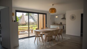 Een moderne keuken met een groot eiland, een eethoek met een houten tafel en stoelen, en uitzicht op de achtertuin door een schuifdeur.