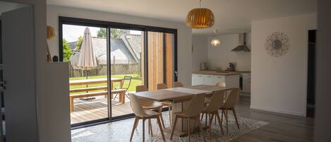 A modern kitchen with a large island, a dining area with a wooden table and chairs, and a view of the backyard through a sliding glass door.