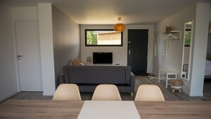 Een moderne woonkamer met een grijze bank, een flatscreen-tv en een eettafel met stoelen.