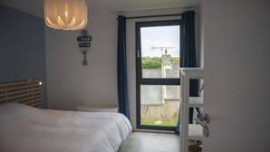 Ein Schlafzimmer mit Bett, einem Fenster mit Vorhängen, einer Hängelampe und einem an der Wand befestigten Schild.