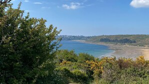 Eine Küstenlandschaft mit blauem Himmel, sandigem Strand und einem steinigen Pfad zum Meer.