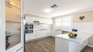 A modern kitchen with white cabinetry, a built-in oven, microwave, and dishwasher. - Dolphin Lagoon, 196 Soldiers Pt Rd - Luxury Escape (Salamander Bay)