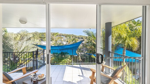 A balcony with a view of a pool, palm trees, and a blue canopy. - Dolphin Lagoon, 196 Soldiers Pt Rd - Luxury Escape (Salamander Bay)