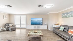 A living room with a large flat-screen TV, a grey sofa, a coffee table, and a window with blinds. - Dolphin Lagoon, 196 Soldiers Pt Rd - Luxury Escape (Salamander Bay)