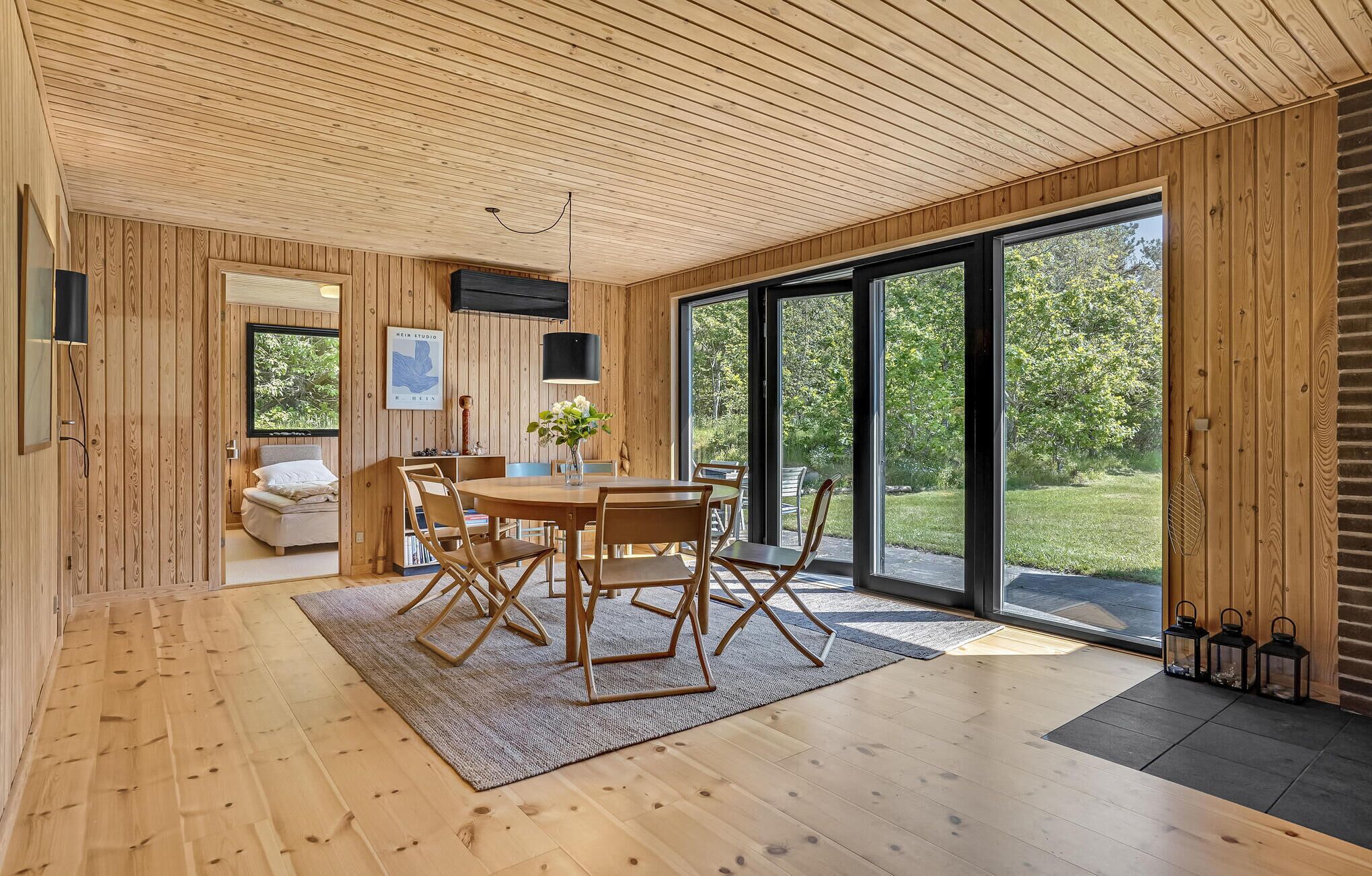 A modern interior with a wooden ceiling, large sliding glass doors, a dining area with a table and chairs, and a cozy seating area with a sofa and a TV.