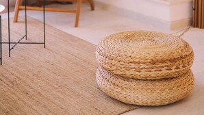 Ein gemütliches Wohnzimmer mit Kamin, einem Korbsessel, einem Weidenhocker und einem kleinen Tisch mit Glas und Flasche.