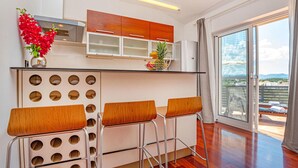 Une cuisine moderne dotée d’un îlot central, de trois tabourets de bar et offrant une vue sur l’extérieur grâce à une porte-fenêtre coulissante.