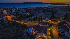 Un quartier résidentiel situé sur la côte, au crépuscule, avec des maisons, une route sinueuse et une étendue d’eau en arrière-plan.