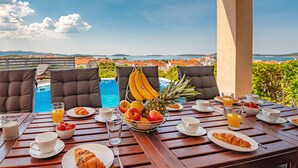 Une table de petit-déjeuner avec des croissants, des fruits et du jus, donnant sur une piscine et un paysage magnifique.