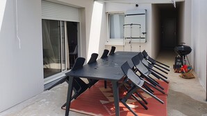 Une terrasse avec une table et des chaises, un barbecue et un étagère de rangement.