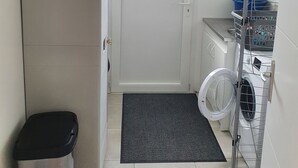 Un espace buanderie comprenant un lave-linge, un étendoir et une poubelle.