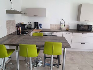 A modern kitchen with a dining table, green chairs, a built-in oven, and a microwave.