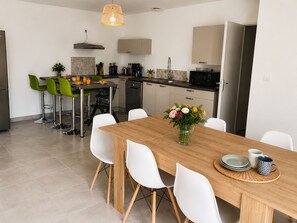 Une cuisine moderne avec un coin repas, comprenant une table en bois, des chaises blanches et un vase de fleurs.