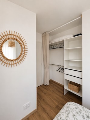 Een slaapkamer met een houten vloer, een witte garderobe met planken, een hangmand en een spiegel aan de muur.