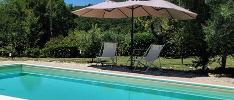 A swimming pool with two lounge chairs and a large umbrella.