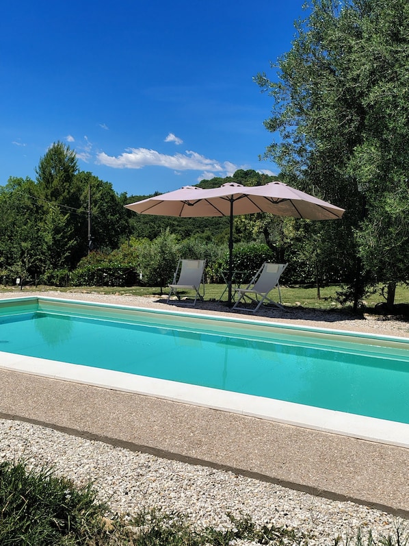 A swimming pool with two lounge chairs and a large umbrella.